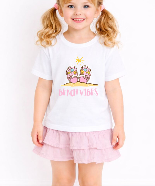 Child wearing a white t-shirt with a beach-themed design and pink shorts on a white background