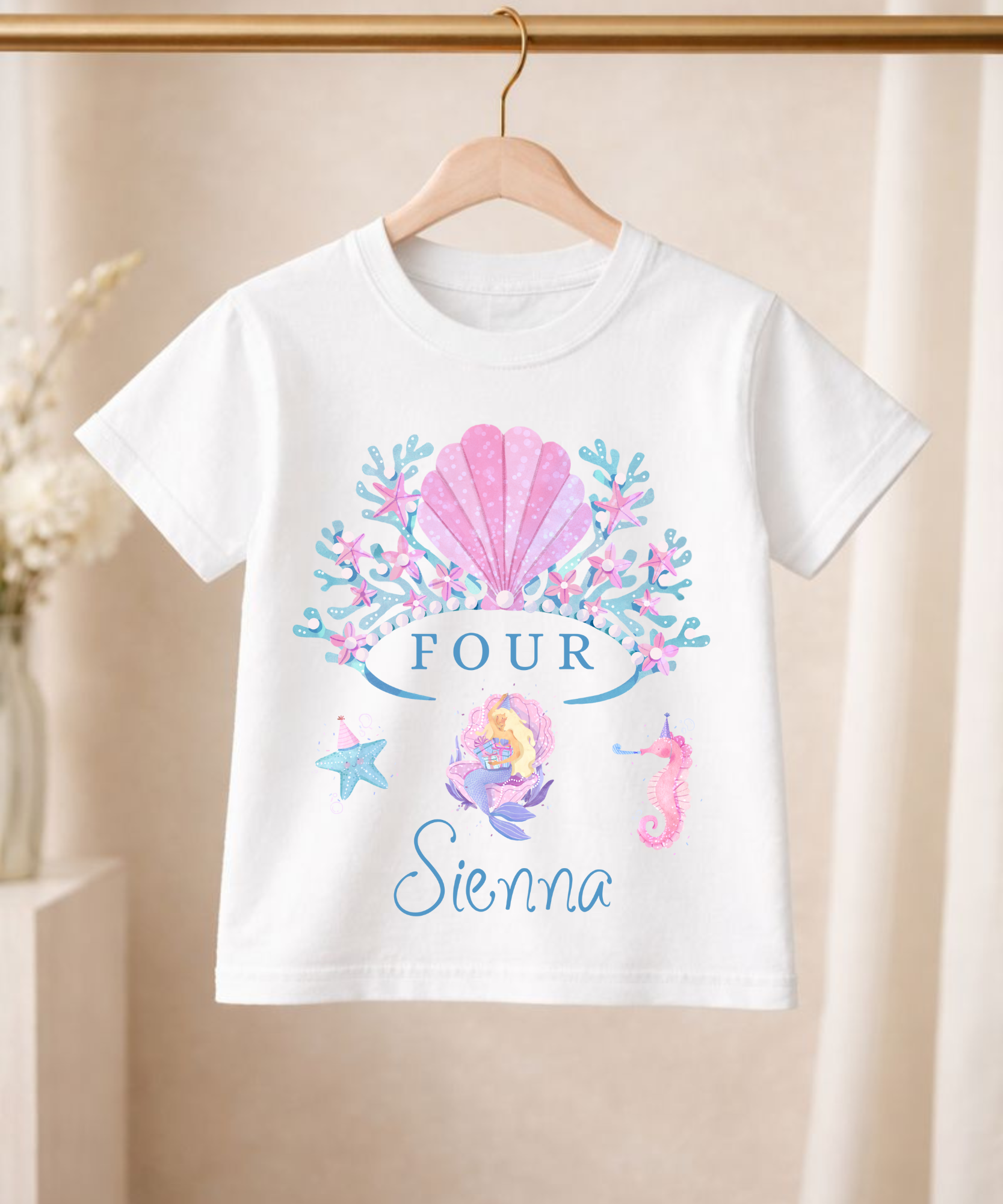 White t-shirt with mermaid-themed design and 'Sienna' on a hanger against a beige background