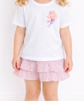 Child wearing a white t-shirt with a cartoon character and a pink ruffled skirt on a plain background