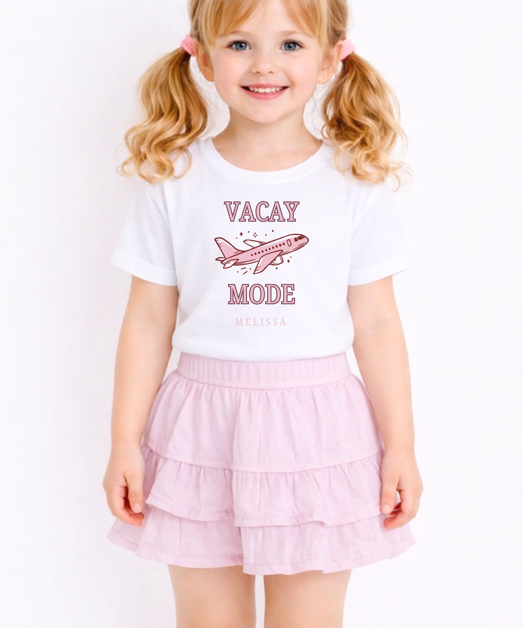 Young girl wearing a white t-shirt with 'Vacay Mode' text and pink airplane graphic, paired with a pink skirt.