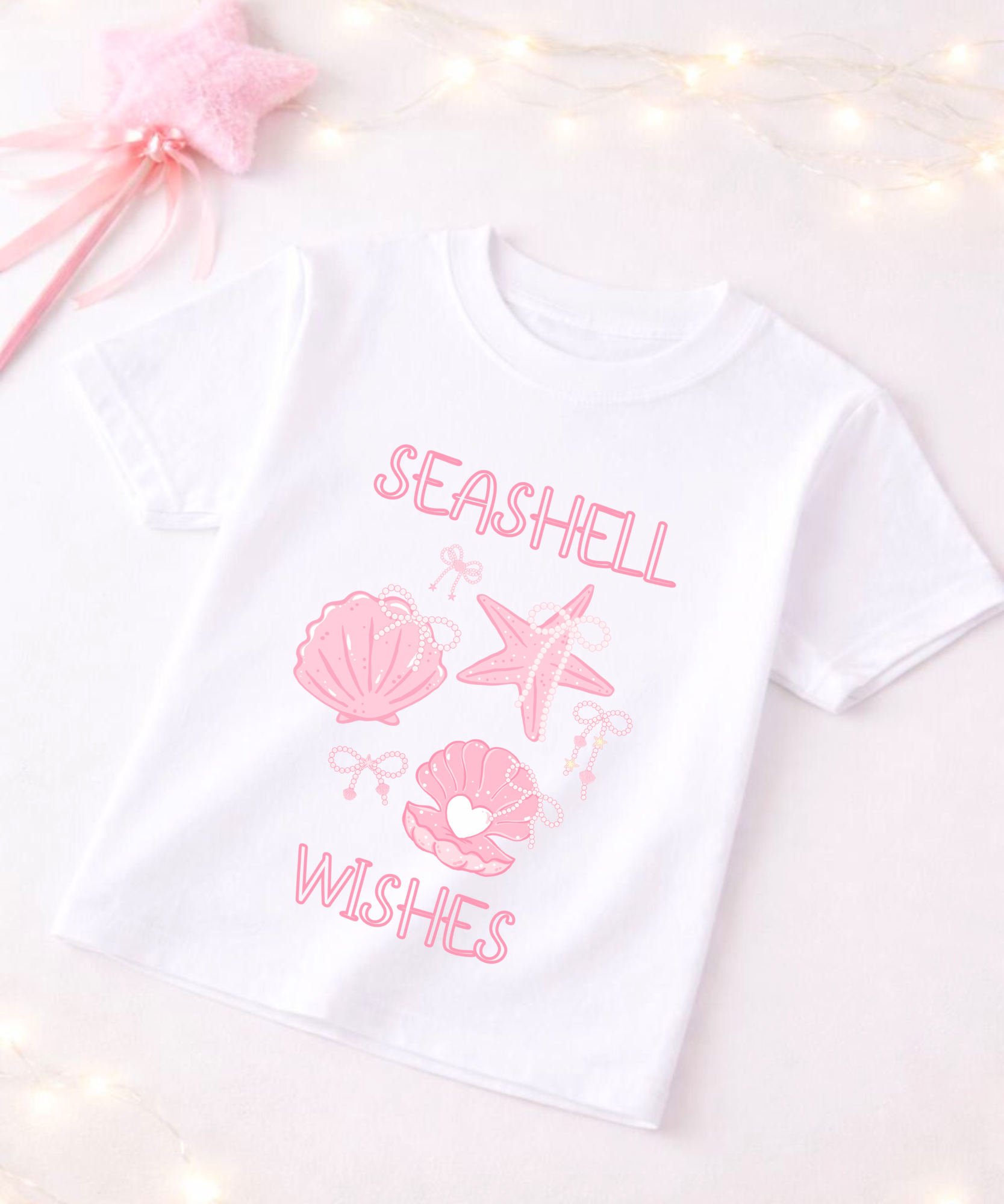 White t-shirt with pink seashell and starfish graphics and text on a white background
