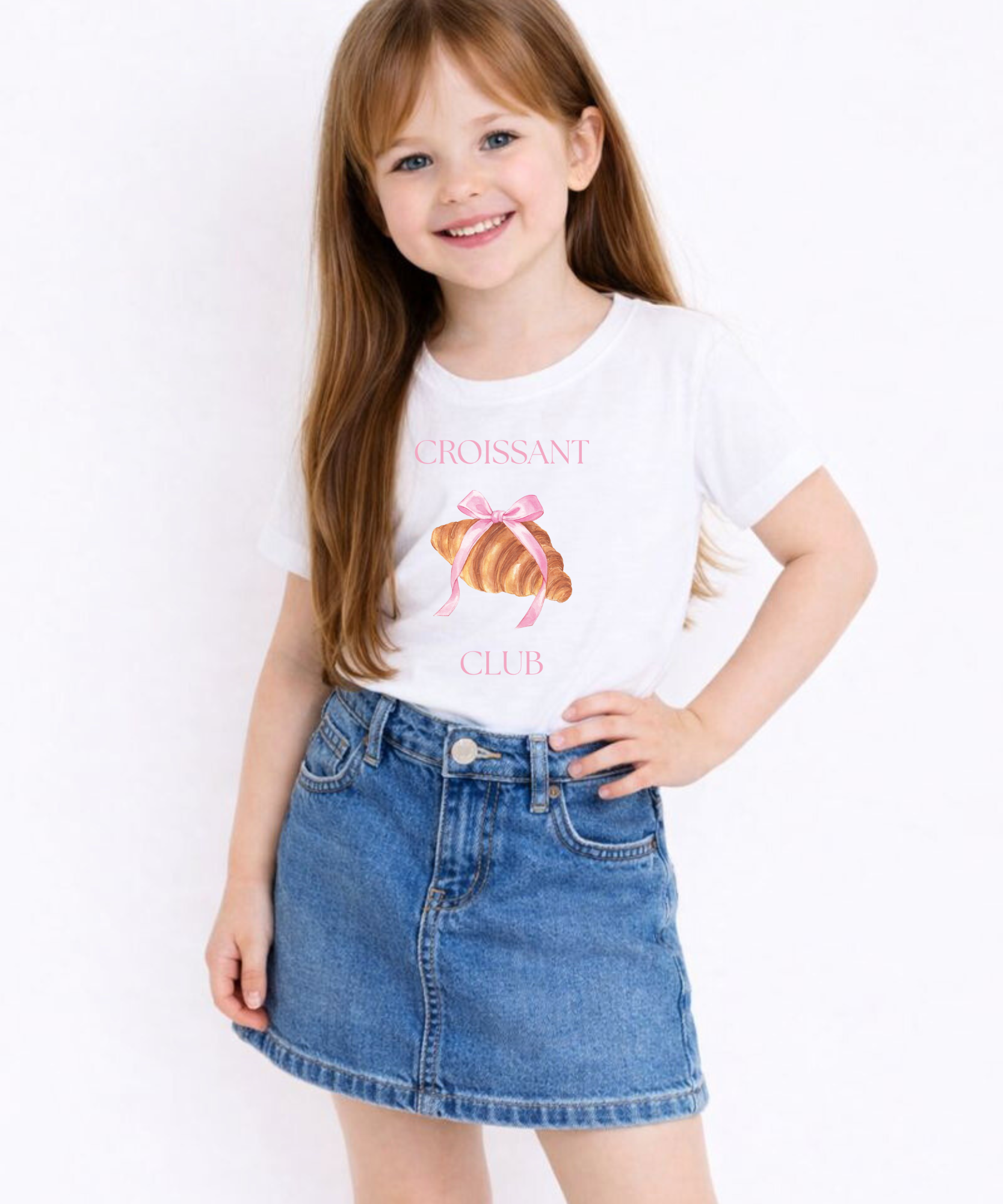 Young girl wearing a white t-shirt with a croissant design and text, standing against a plain background.